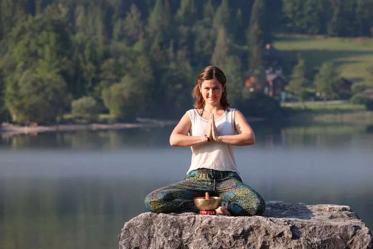 Hier sehen Sie unsere Yoga-Lehrerin Martina Schorn auf einem Stein am See!